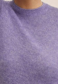 Pull en tricot violet avec un col rond et une texture douce, présentant un motif uniforme et des poignets côtelés.