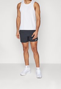 Top deportivo sin mangas blanco, pantalones cortos negros con logo y zapatillas deportivas blancas. Diseño simple, materiales ligeros y colores neutros.