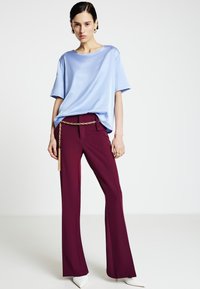 Maglietta di raso azzurro chiaro con vestibilità ampia, abbinata a pantaloni sartoriali bordeaux con cintura a catena. Scarpe con tacco bianche a punta.