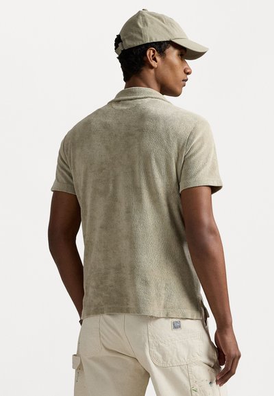 Polo à manches courtes en tissu éponge beige clair, avec une texture douce et un col classique. Assorti à une casquette, avec des accents en métal visibles.