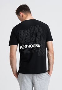 Svart bomull t-shirt med en djärv "PENTHOUSE"-logga i vitt, omgiven av upprepad text i grått. Klassisk rund hals och avslappnad passform.