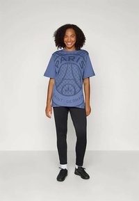 T-shirt bleu oversize avec les textes "PARIS" et "SAINT-GERMAIN", agrémenté d'un graphisme texturé de la Tour Eiffel. Associé à un legging noir et des chaussures.