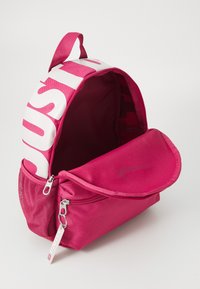 Rosa ryggsäck med rundad form, tillverkad av hållbart material. Har en stor vit "JUST DO IT"-logotyp och en framfick med dragkedja.