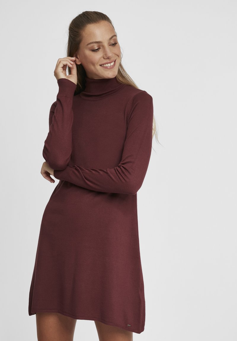 Robe turtleneck bordeaux à manches longues, à coupe décontractée, avec des fentes sur les côtés. Texture douce, col et poignets côtelés, avec un petit accent métallique.