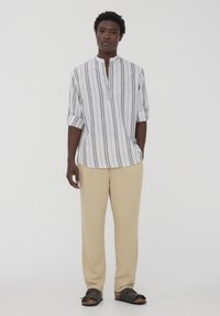 Maglietta a maniche lunghe bianca e grigia a righe con colletto zip, abbinata a pantaloni beige e sandali neri. Vestibilità casual e tessuto leggero.