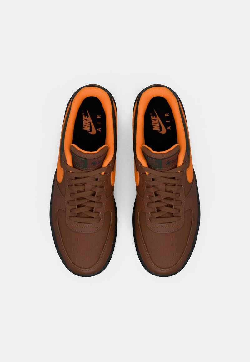 Baskets Nike Air marron avec des accents orange, une tige texturée, un bout rond et une semelle en caoutchouc noir. Lacets et détails du logo inclus.