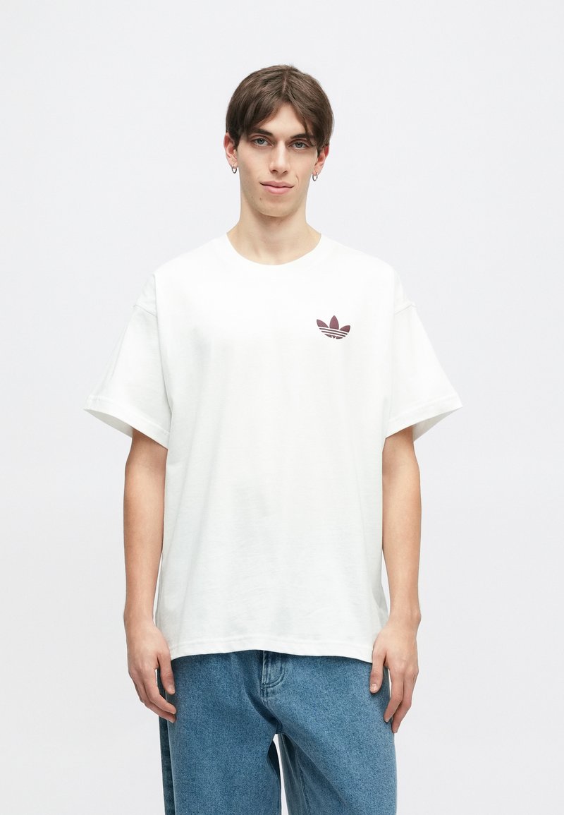 Witte katoenen t-shirt met een ronde halslijn, korte mouwen en een maroon Adidas-logo op de borst. Draagt met lichtblauwe denim jeans.