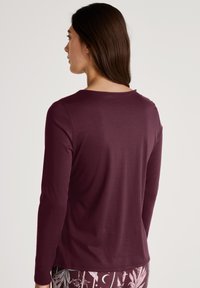 Langsleeve, bordeaux top van zachte stof met een ronde halslijn. Heeft een gladde textuur en een minimalistisch ontwerp, gezien vanaf de achterkant.