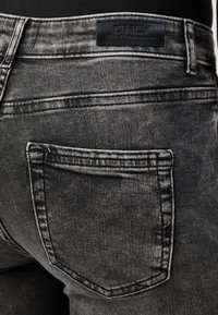 Jeans de mezclilla negros con una textura desgastada, múltiples detalles de costura y un bolsillo trasero con una etiqueta que dice "ONLY Blue Cont."