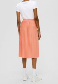 Falda midi plisada en suave tono melocotón, con una cinturilla ancha, tela ligera, combinada con una camiseta blanca y zapatillas blancas.