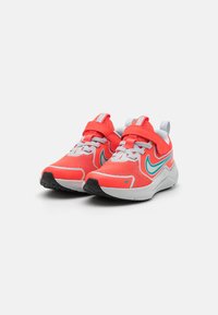 Baskets de sport avec une tige en mesh corail vibrant, accents gris, logo swoosh bleu et col rembourré. Présentent une sangle velcro sécurisée.