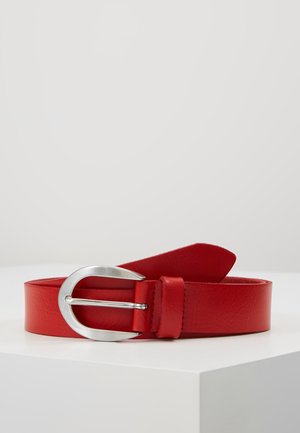 Rode leren riem met een zilveren, ronde metalen gesp, opgerold op een witte ondergrond tegen een effen lichte achtergrond.