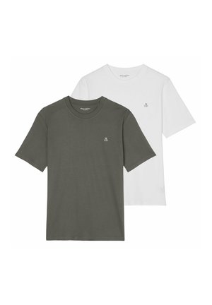 Nahaufnahme einer Person, die ein weißes Hemd mit kleinen schwarzen Buchstaben "M O'P" in der Nähe des Brustbereichs trägt.