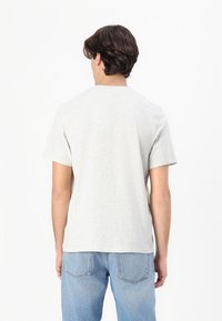 T-shirt corto grigio chiaro con maniche corte e collo rotondo, realizzato in cotone morbido, indossato da una persona con jeans blu. Design semplice, senza motivi.