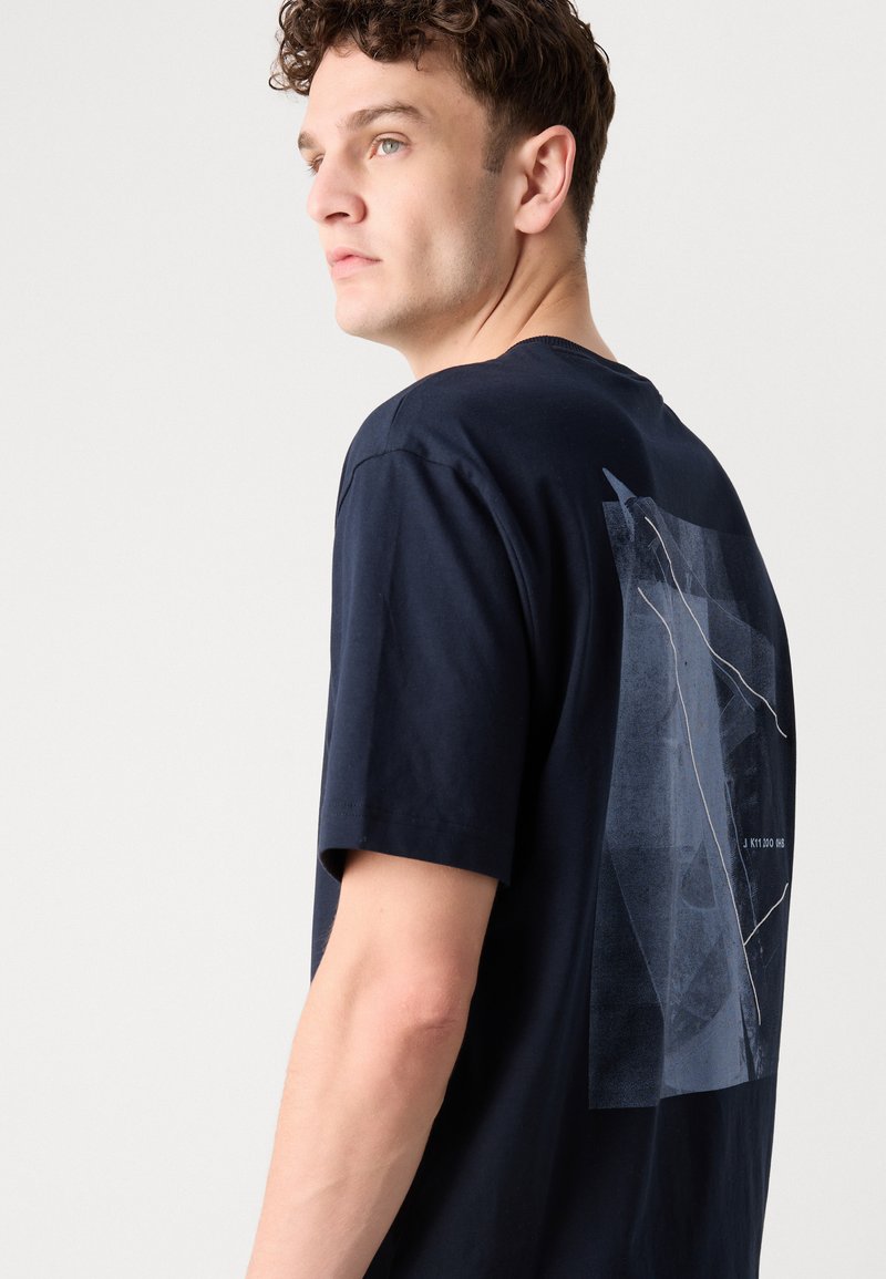 Camiseta de algodón azul marino con un diseño gráfico en la parte posterior, que incluye formas y líneas abstractas en tonos de azul claro. Mangas cortas.