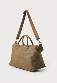 Sac de voyage en cuir marron avec une forme structurée, deux poignées supérieures et une bandoulière réglable. Présente une texture lisse et une fermeture éclair.