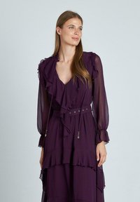 Vestido morado de manga larga con detalles de volantes, escote en V, cintura ceñida y dobladillo en capas. Hecho de tela ligera con una textura fluida.
