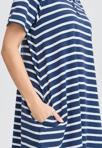 Abito a strisce blu navy e bianche con maniche corte e vestibilità ampia, dotato di due tasche laterali e un doppio bottone sul collo.