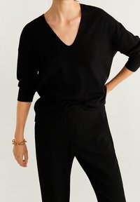 Black, soft knit sweater with a deep V-neck and three-quarter sleeves, paired with black tailored pants. Simple, minimal design.