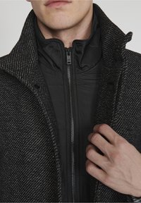 Teksturowany czarno-szary płaszcz w wzory z wysokim kołnierzem, z zamkiem z przodu i gładką czarną podszewką.