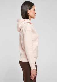 Lyserød hættetrøje lavet af blødt stof, med en kengurupose, to-tone snore og ribbede cuffs. Stylet med brune leggings.