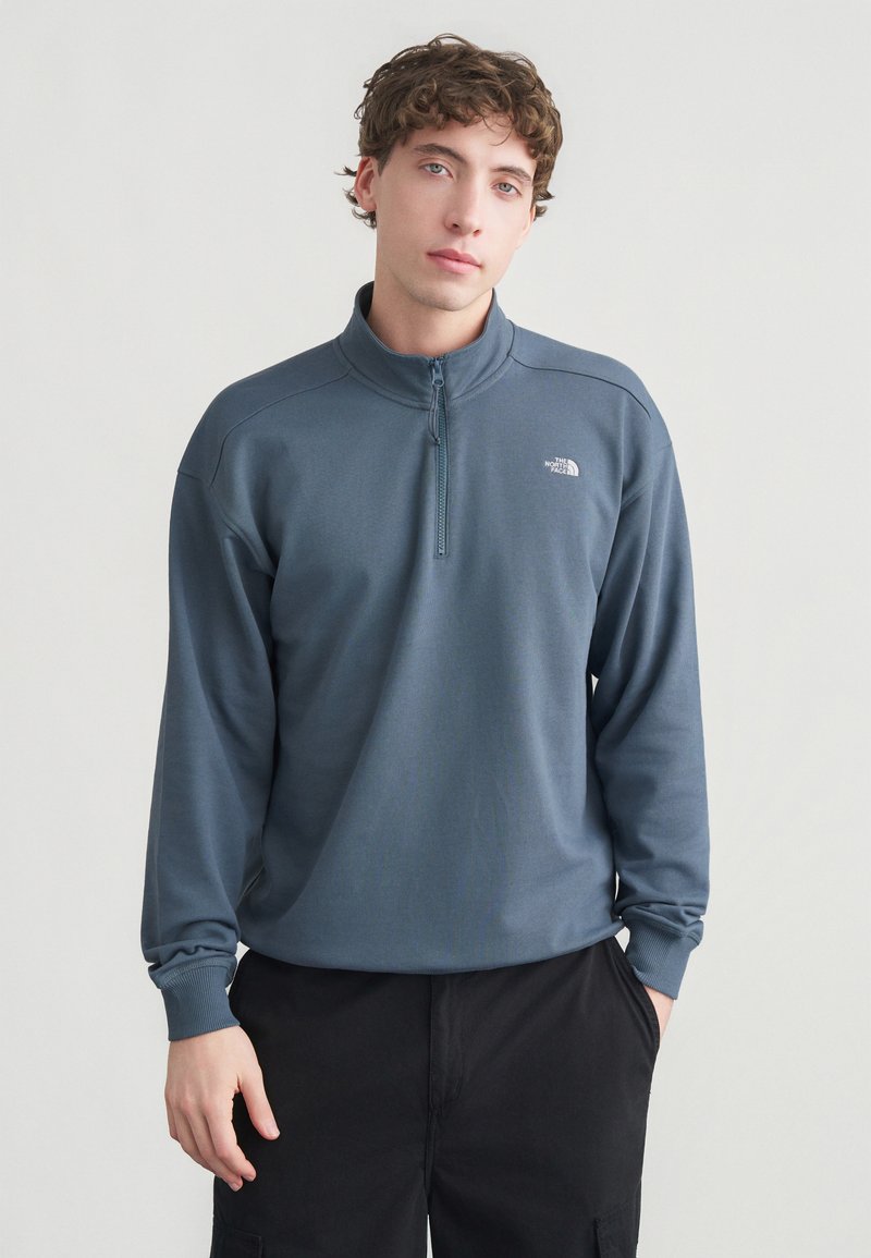 Fleece pullover in blue-gray with a half-zip collar and long sleeves. Features a subtle texture and a logo on the chest. Casual fit.