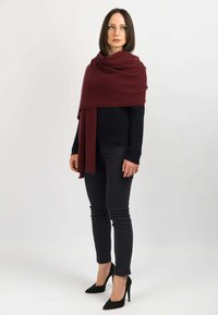En bordeaux sjal lagt over en navy top, parret med sorte skinny bukser og spidse sorte hæle, hvilket skaber en lagdelt effekt. Glat tekstur.