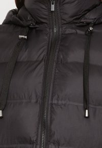 Svart pufferjacka med dragkedja, med justerbara dragsko och quiltad textur. Slät, lättviktsmaterial.