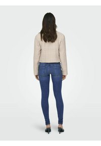 Chaqueta corta beige con una superficie texturada, combinada con jeans ajustados azul. Los jeans cuentan con bolsillos traseros y un diseño ceñido.