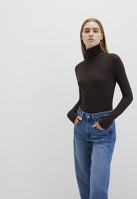 Long-sleeve, dark brown turtleneck top paired with high-waisted, light blue jeans. The shirt features thumbholes in the cuffs.