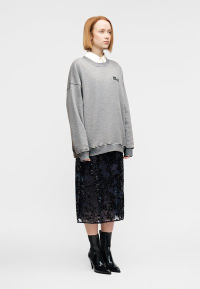 Υπερμεγέθη γκρι φούτερ με ριμπ μανσέτες, φορεμένο πάνω από μαύρη midi φούστα με παγιέτες. Στενά μαύρα μποτάκια με ψηλό τακούνι και λευκό πουκάμισο με γιακά.