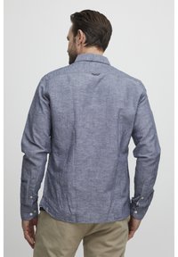 Camicia blu in chambray a maniche lunghe con polsini a bottoni, colletto a punta e un dettaglio ad anello sul collo; tessuto texture con un motivo sottile.