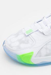 Baskets blanches avec dessus en mesh, détail de boucle verte, et semelle translucide bleue et verte, vues en gros plan de côté.