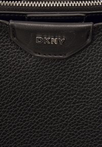 Černá kabelka DKNY s texturovaným koženým povrchem. Obsahuje zipové zavírání a kovový logový štítek na přední straně. Kompaktní design.