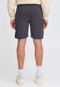 Shorts gris mi-cuisse en tissu doux, dotés d'une poche arrière, d'une taille élastique et d'une coupe décontractée. Portés avec des chaussettes blanches et des chaussures.