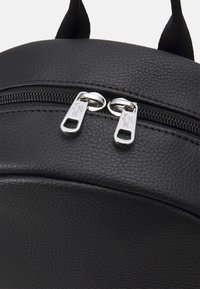 Black synthetic leather backpack with a curved shape, featuring dual silver zipper pulls and textured surface. Limited visible stitching detail.