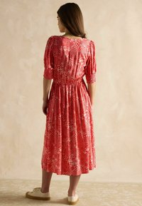 Rotes Blumenkleid aus leichtem Stoff mit kurzen, puffigen Ärmeln, elastischem Taillenbund und Midi-Länge. Akzentuiert mit weißen Blumenmustern.