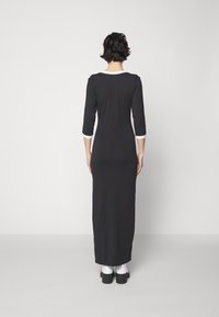 Svart klänning med lång ärm och åtsittande silhuett, vit accent vid ärmsluten och halsringning, tillverkad av mjukt tyg som når anklarna.