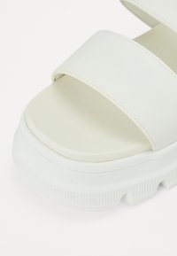Sandalo platform bianco con due ampie cinturini realizzati in materiale liscio e opaco. Suola in gomma spessa e testurizzata per aderenza e resistenza.