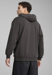 Felpa grigia scura in tessuto strutturato, con un cappuccio ampio e polsini a coste. La parte posteriore presenta un design pulito e ininterrotto.