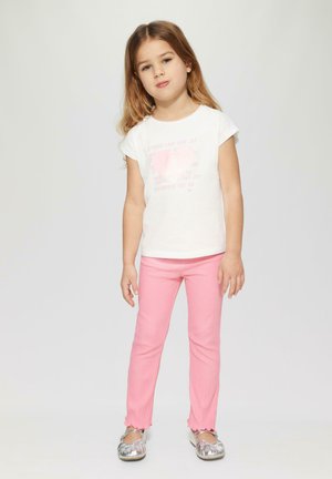 Weißes Kurzarmhemd mit pinkem Herz-Graphic-Text, kombiniert mit pinken gerippten Leggings und silbernen flachen Schuhen mit abgerundetem Zeh.