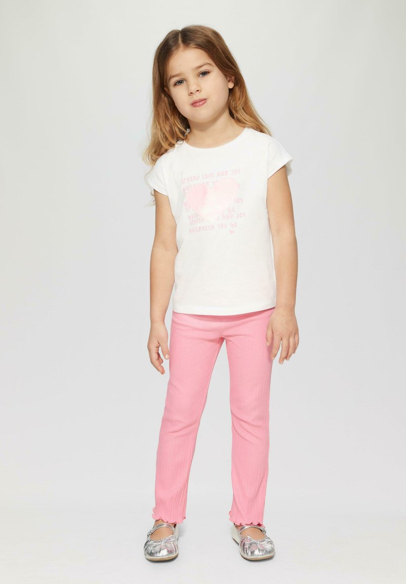 Witte T-shirt met korte mouwen met een roze hart grafische tekst, gecombineerd met roze geribde leggings en zilveren platte schoenen met een ronde neus.