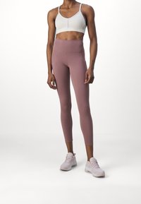 Soutien-gorge de sport gris clair et legging rose en tissu extensible, avec une taille haute et un design ajusté. Baskets de sport rose clair.