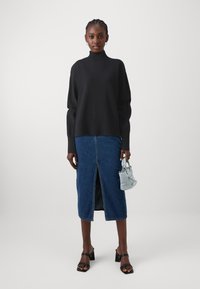 Pull en maille côtelée noir à col roulé, jupe midi en denim avec fente à l'avant, sandales à talons bloc noires et petit sac à main bleu clair.