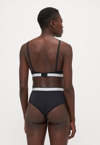 Conjunto de lingerie preto com um bralette de alças ajustáveis e uma parte de baixo de cintura alta, ambos com uma faixa branca em contraste.