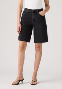 Zwarte denim shorts met een rechte snit, hoge taille, voorzakken en subtiele vervaging, gecombineerd met zwarte sandaaltjes met banden.