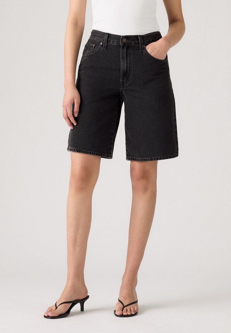 Zwarte denim shorts met een rechte snit, hoge taille, voorzakken en subtiele vervaging, gecombineerd met zwarte sandaaltjes met banden.