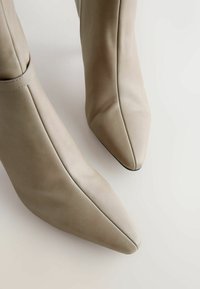 Beige læder ankelstøvler med spids tå, der har et sømløst design og subtile syninger. Glat tekstur.