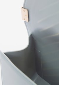 Borsa strutturata azzurro chiaro con finitura in pelle liscia, caratterizzata da una elegante chiusura dorata e un interno aperto con linee e bordi delicati.