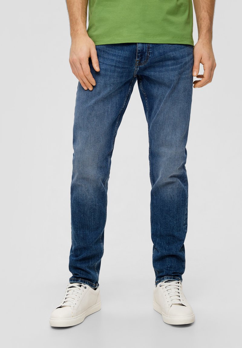 Jeans in denim blu scuro con una vestibilità regolare, caratterizzati da una leggera scoloritura e un classico design a cinque tasche, abbinati a sneakers bianche.
